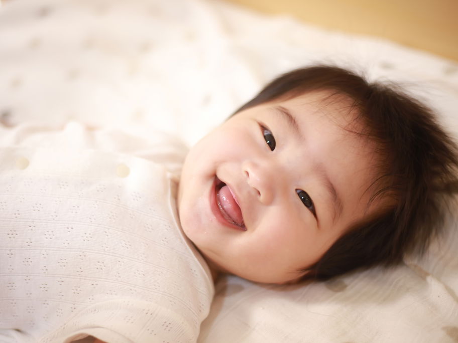 Japanisches Baby liegt lachend im Bett.