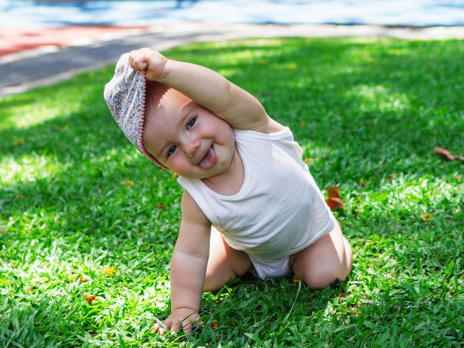 Ein kleines Baby, das sich die Mütze vom Kopf zieht.