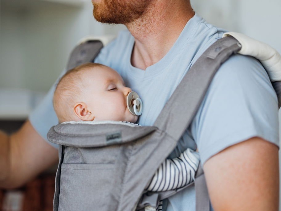 Ein Baby schläft bei Papa in der Trage mit Schnuller