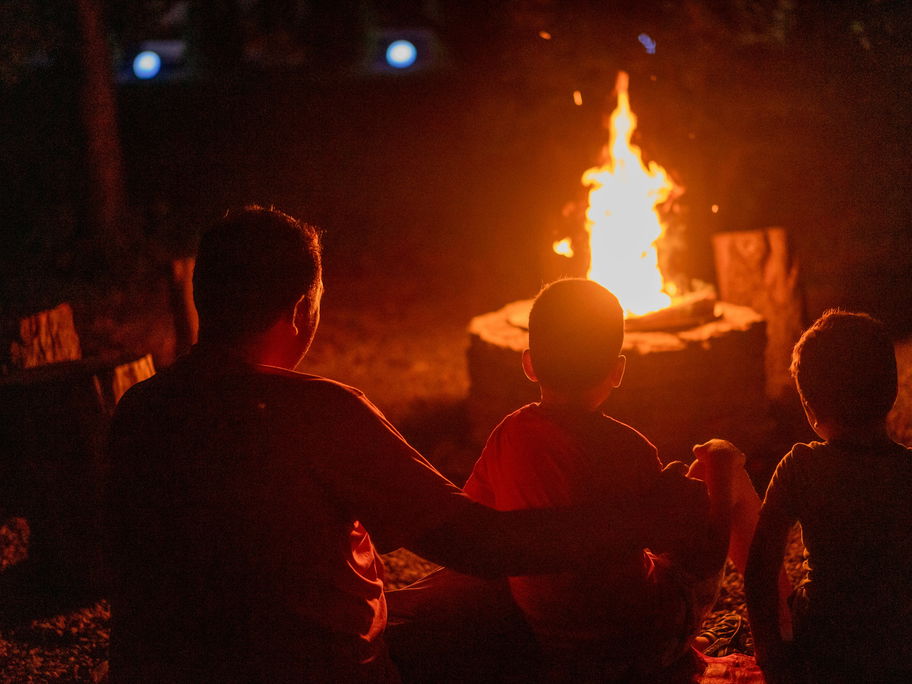 Ein Vater sitzt mit seinen beiden Kindern am Lagerfeuer.