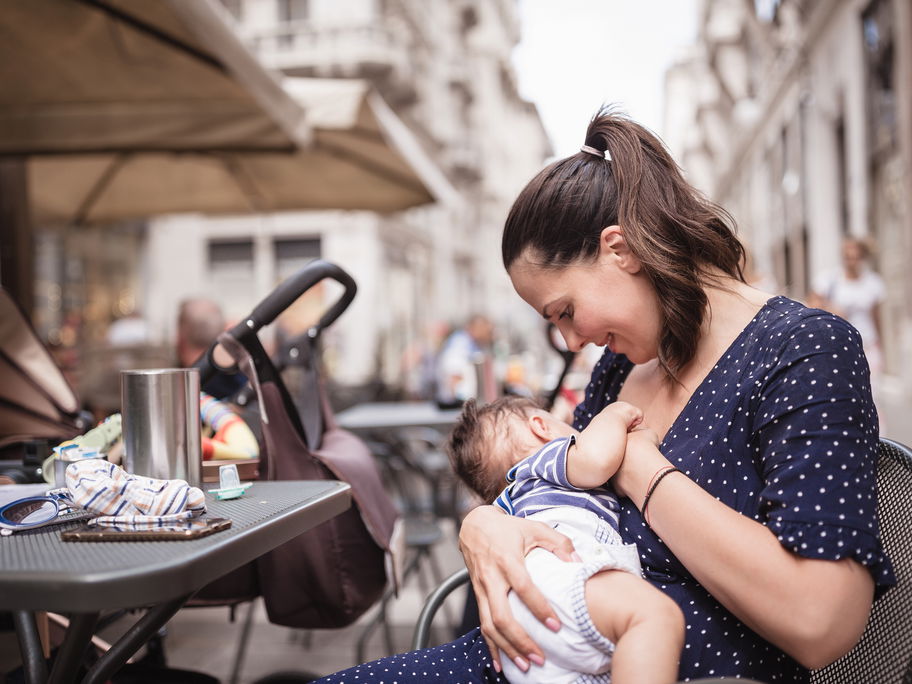 Eine Mutter stillt ihr Baby draußen in einem Café.