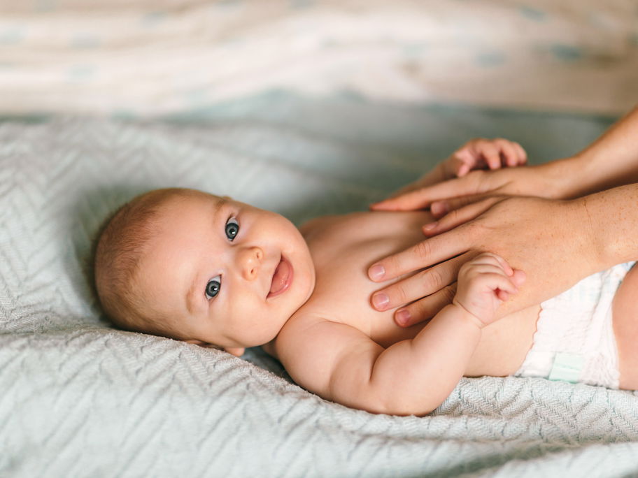Baby liegt lächelnd auf einer Decke.