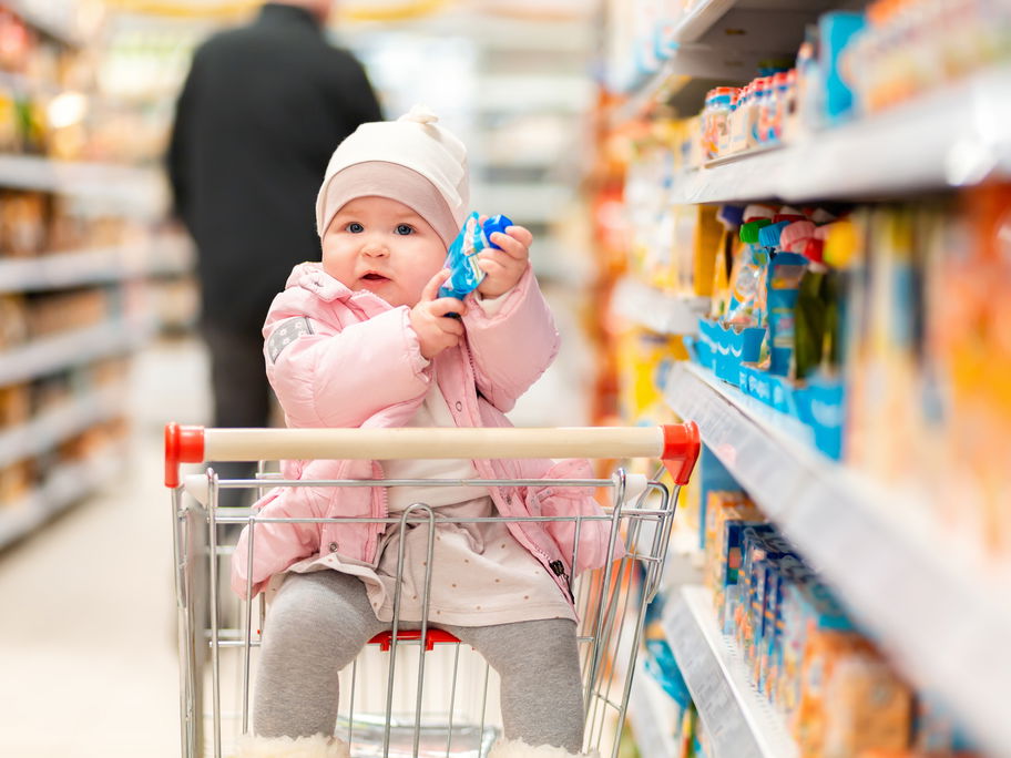 Ein kleines Baby hat in einem Supermarkt einen Quetschie in der Hand.