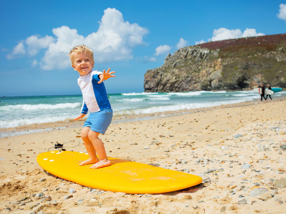 Kleiner Junge steht auf einem Surf-Brett.