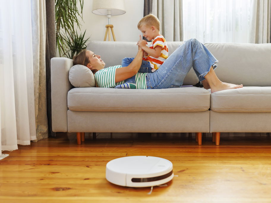 Mutter und Kind sitzen auf dem Sofa vor einem Saug-Roboter.