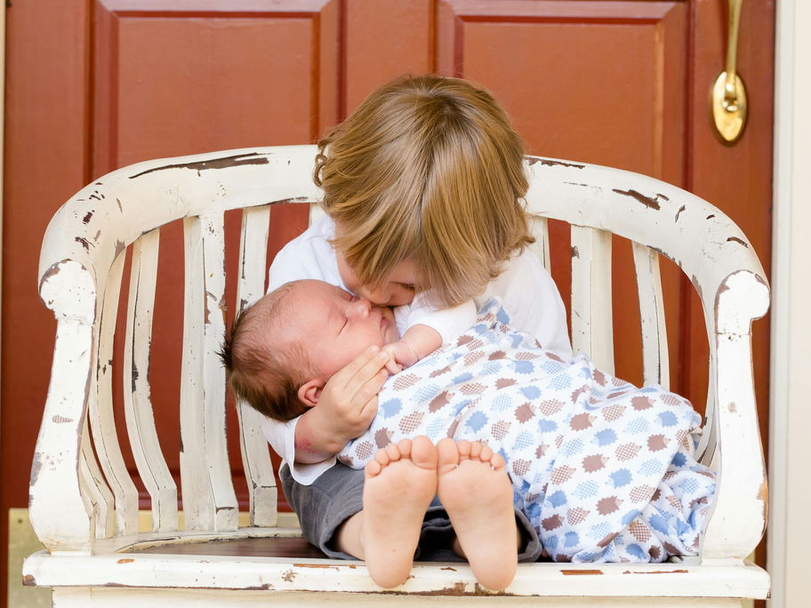 Ein kleiner Junge küsst seine Baby-Schwester, die er im Arm hält.