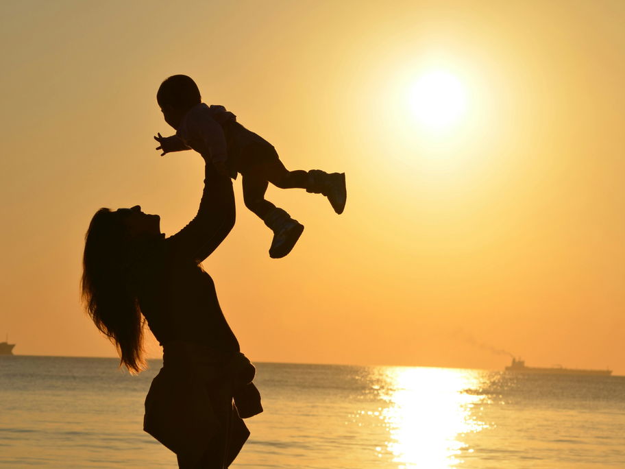Eine Mutter hält ihr Baby beim Sonnenuntergang am Strand in die Luft.