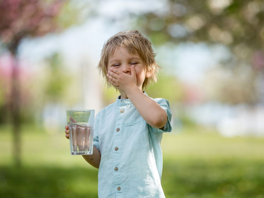 Blonder Junge trinkt Wasser im Park.