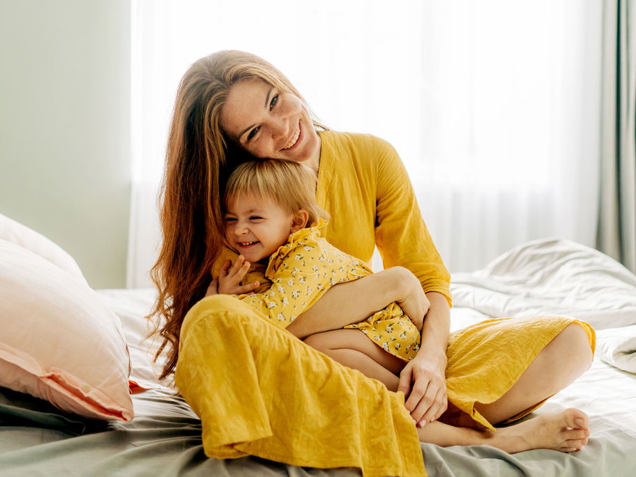 Mama und Kind umarmen sich auf dem Bett.