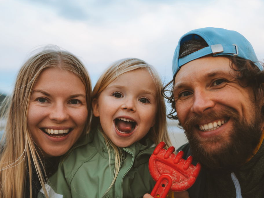 Mama, Papa und Kind lachen in die Kamera.