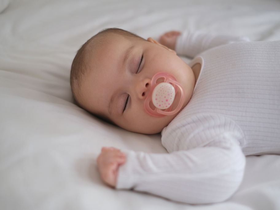 Schlafendes Baby mit Schnuller im Bett