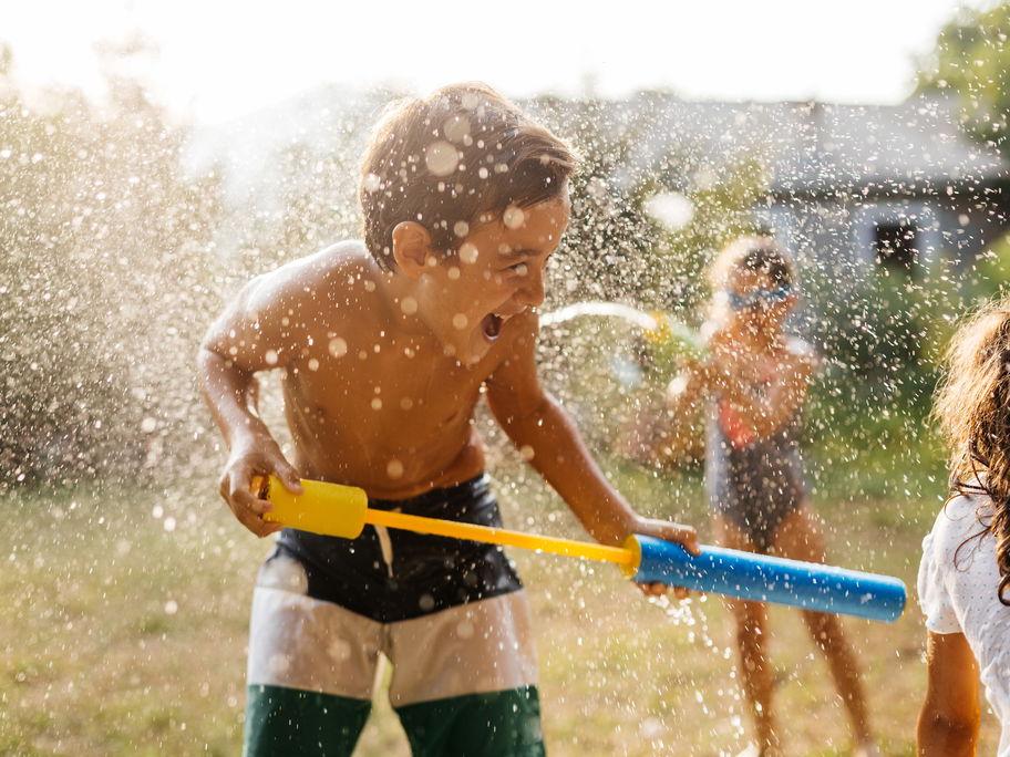 Junge spielt im Garten mit Wasserpistole.