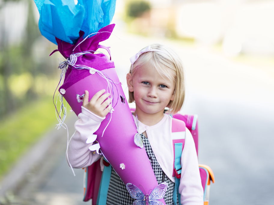 Ein kleines Mädchen hält eine Schultüte in der Hand.