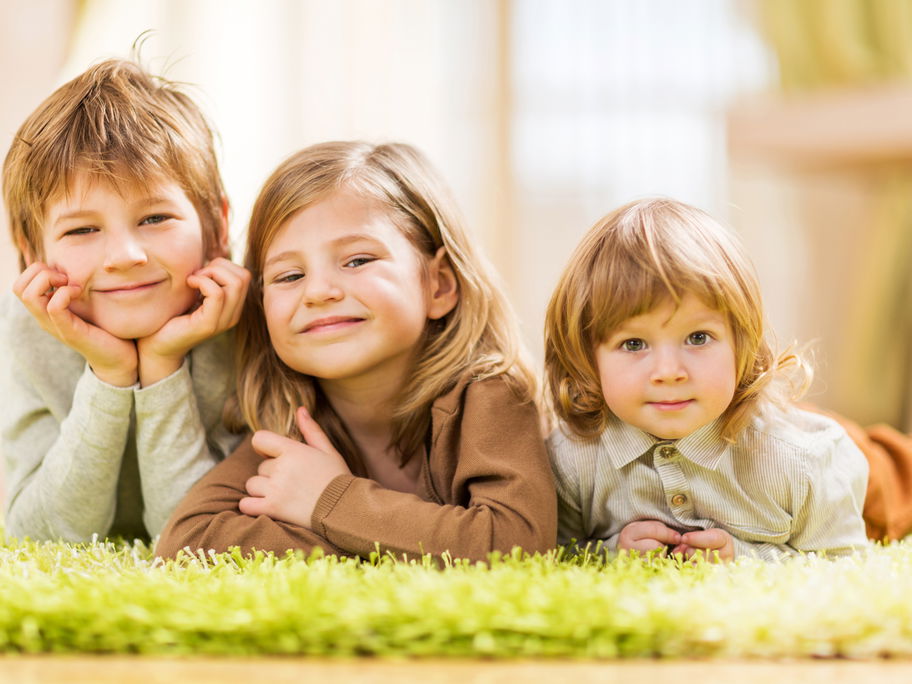 Drei Kinder liegen auf dem Teppich.