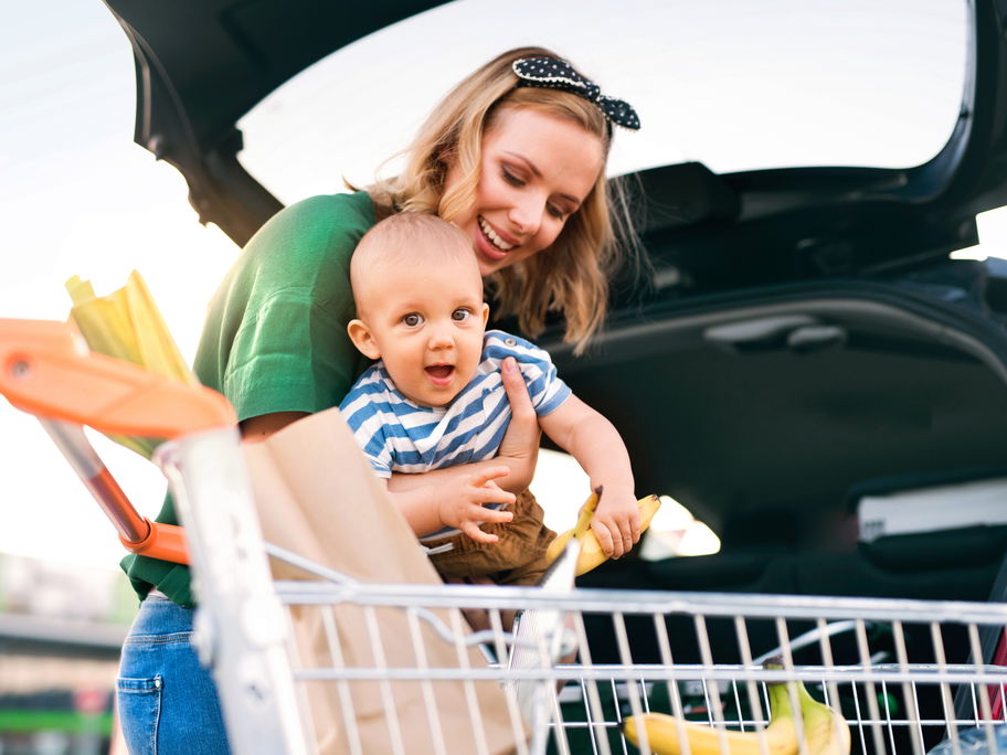 Mutter mit Baby und Einkaufswagen am Auto