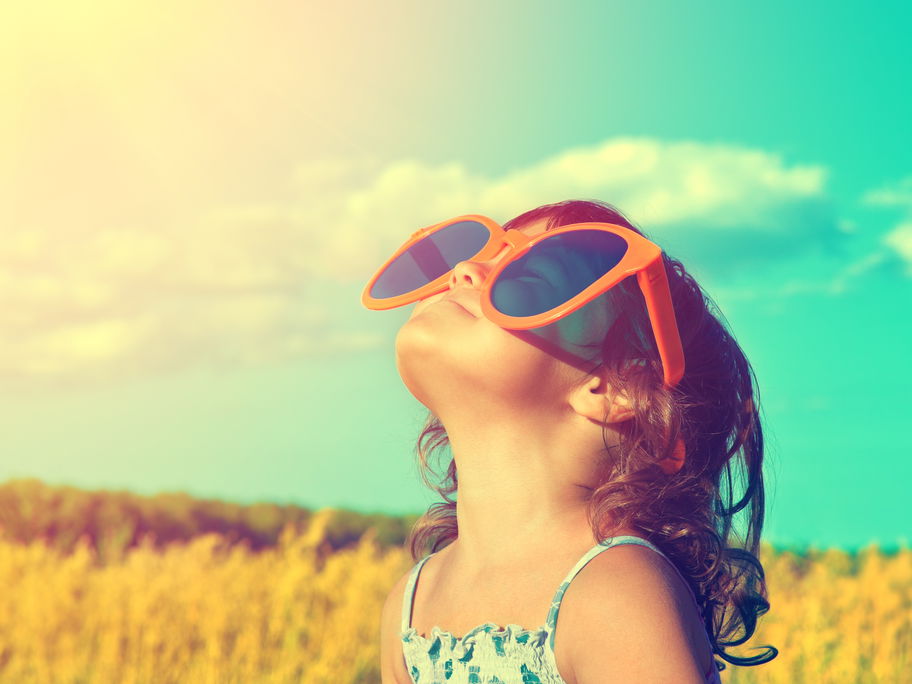 Kind schaut mit riesiger Sonnenbrille in den Himmel.
