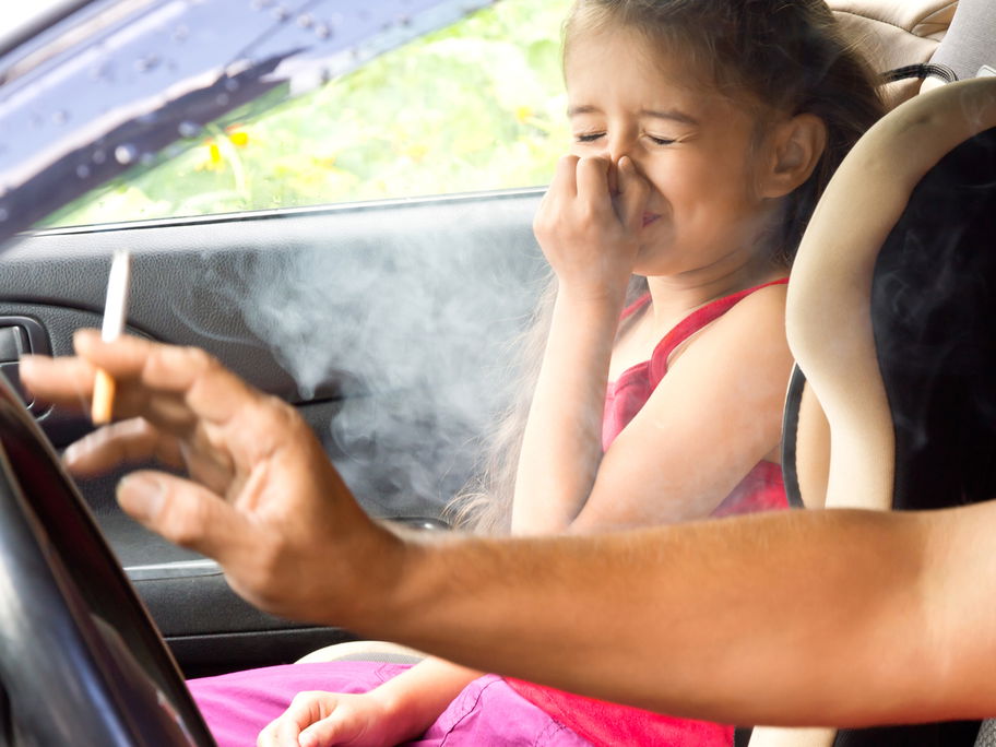 Kind hält sich wegen Zigarrettenrauch im Auto die Nase zu.