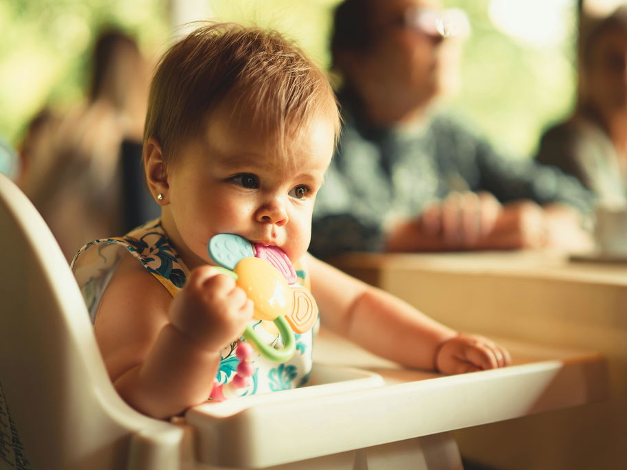 Baby im Hochstuhl kaut auf einem Beißring