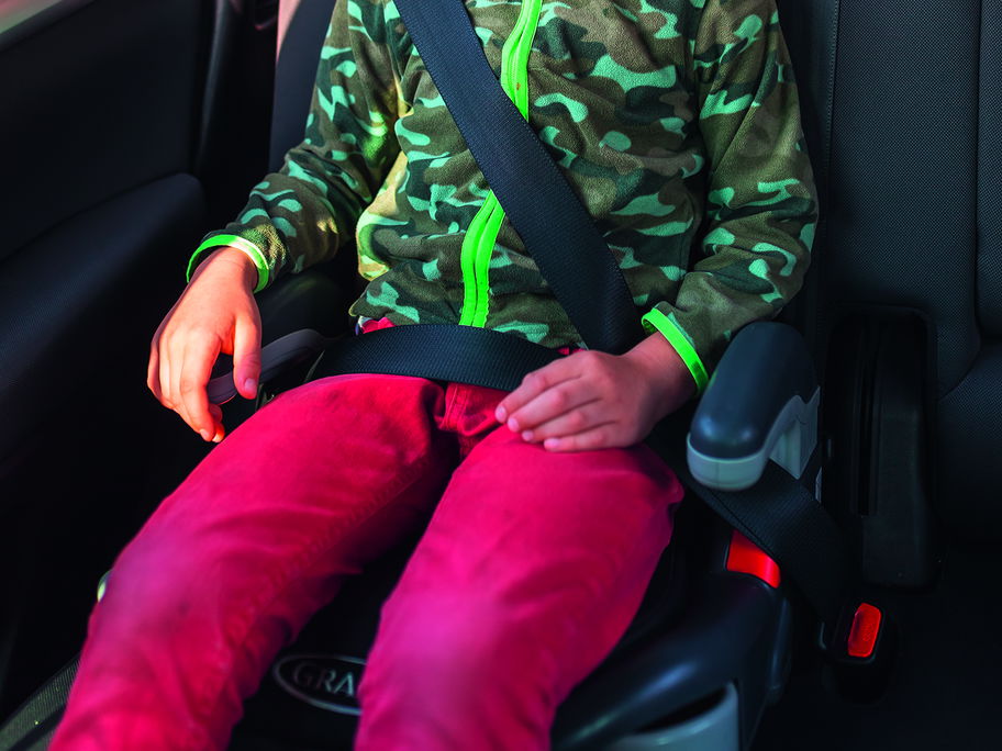 Eine Junge sitzt im Auto auf einer Sitzerhöhung.