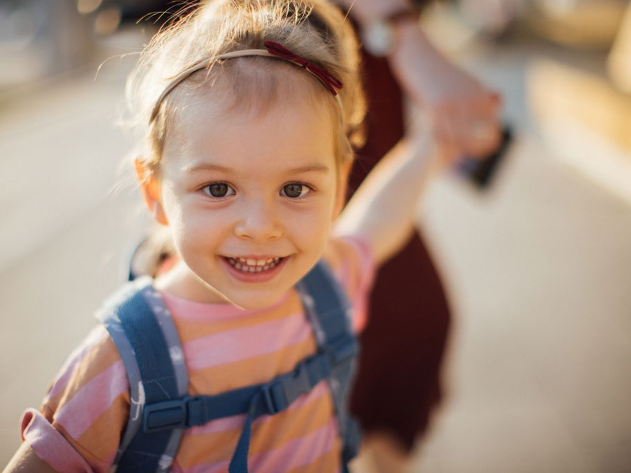 Mädchen mit Kita-Rucksack an der Hand ihrer Mama