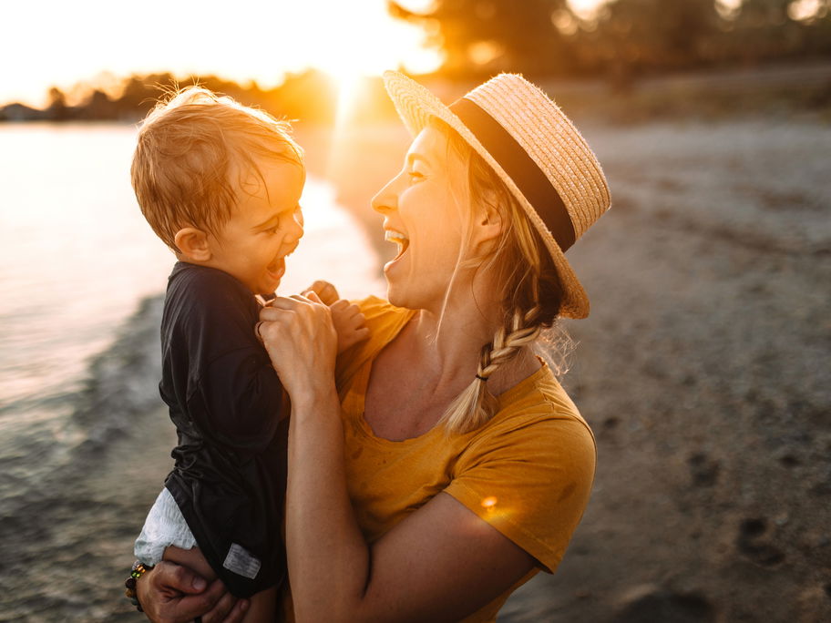 Mutter und Sohn lachend am Strand bei Sonnenuntergang.