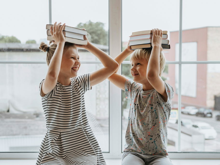 Fröhliche Kinder mit Büchern auf dem Kopf.