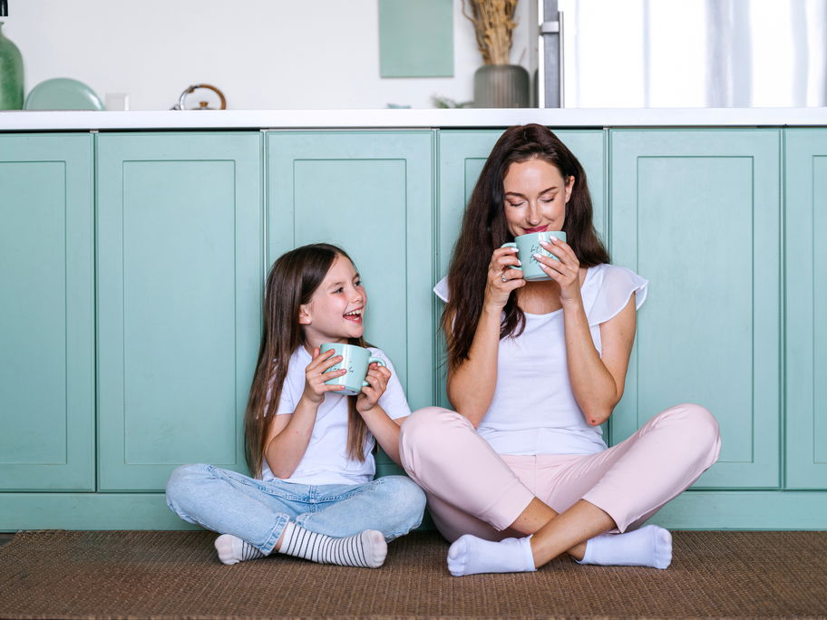 Mama und Tochter sitzen in der Küche und trinken aus Tassen.