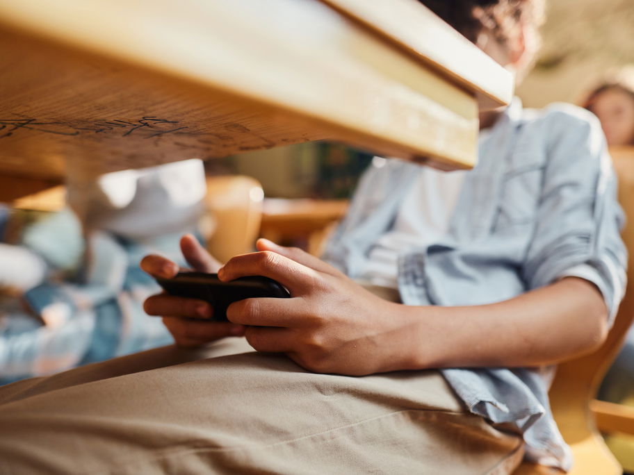 Junge spielt unter dem Schultisch am Smartphone.