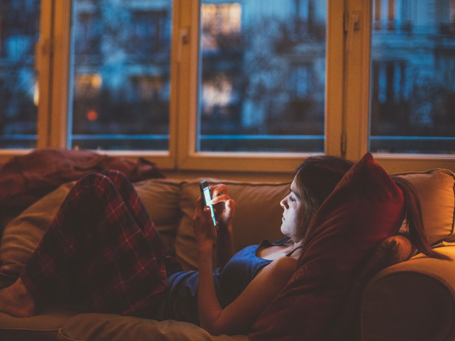 Frau liegt auf dem Sofa und guckt auf ihr Handy.