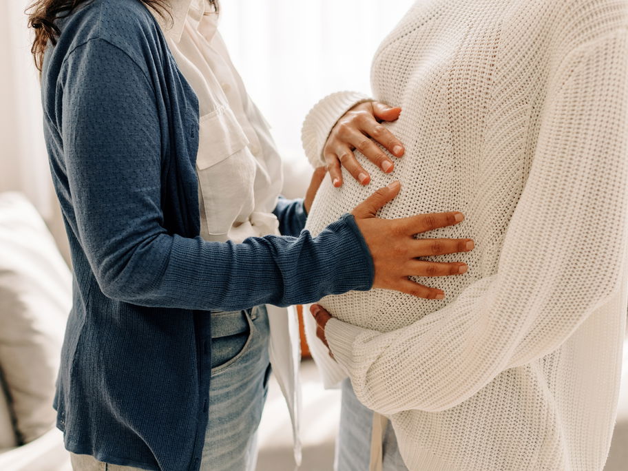 Eine Frau streichelt den schwangeren Bauch einer anderen Frau.