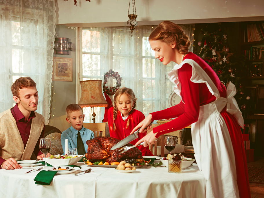 Frau im roten Kleid serviert ihrer Familie einen Braten.