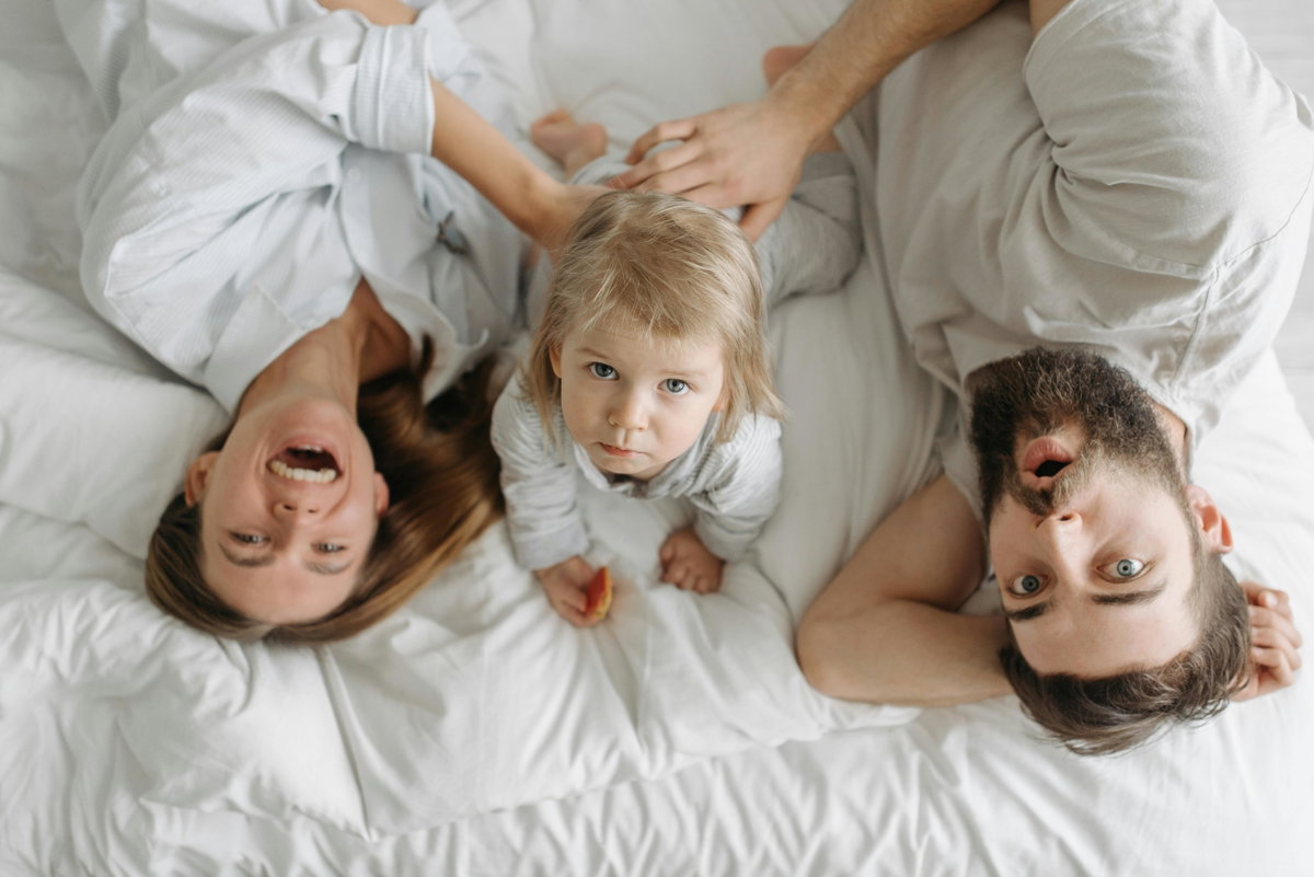 Eltern liegen mit Baby auf dem Bett und machen Quatsch.