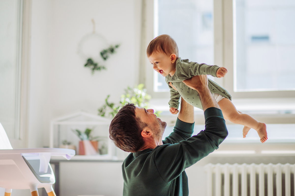 Papa hebt lachendes Baby in die Luft.