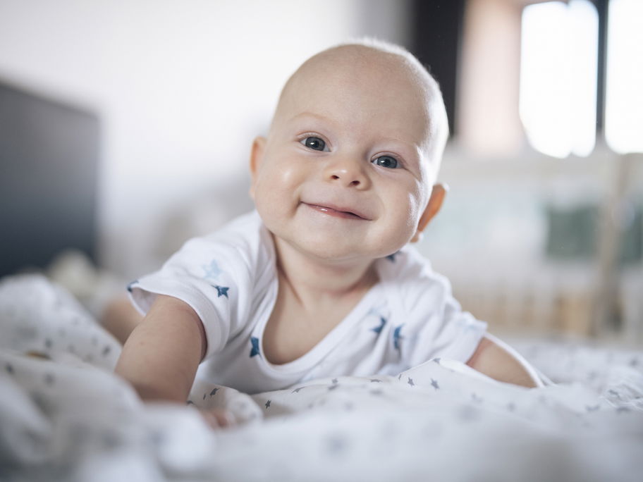 Lächelndes Baby liegt auf dem Bauch.