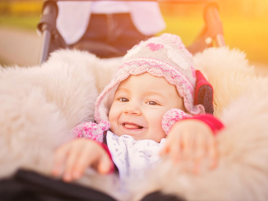 Lachendes Baby in Lammfell-Fußsack im Kinderwagen.