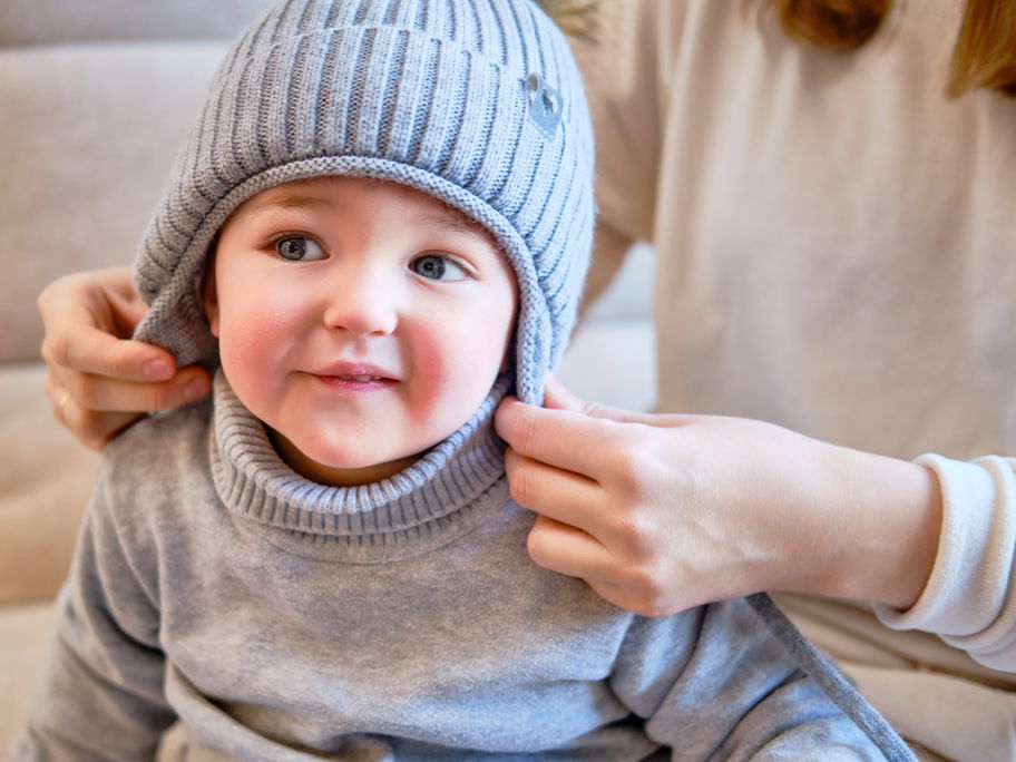Kleinkind bekommt von der Mutter eine Mütze aufgesetzt.