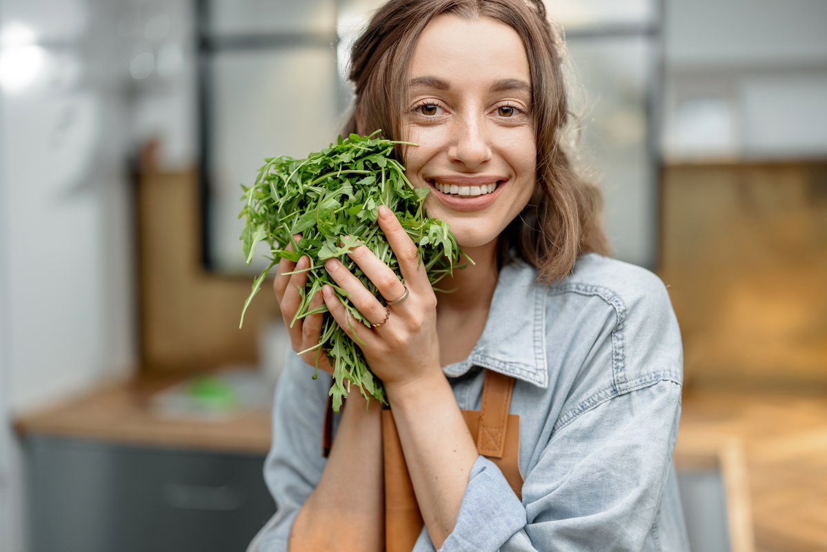 Fröhliche Frau halt einen Büschel Rucola in den Händen.