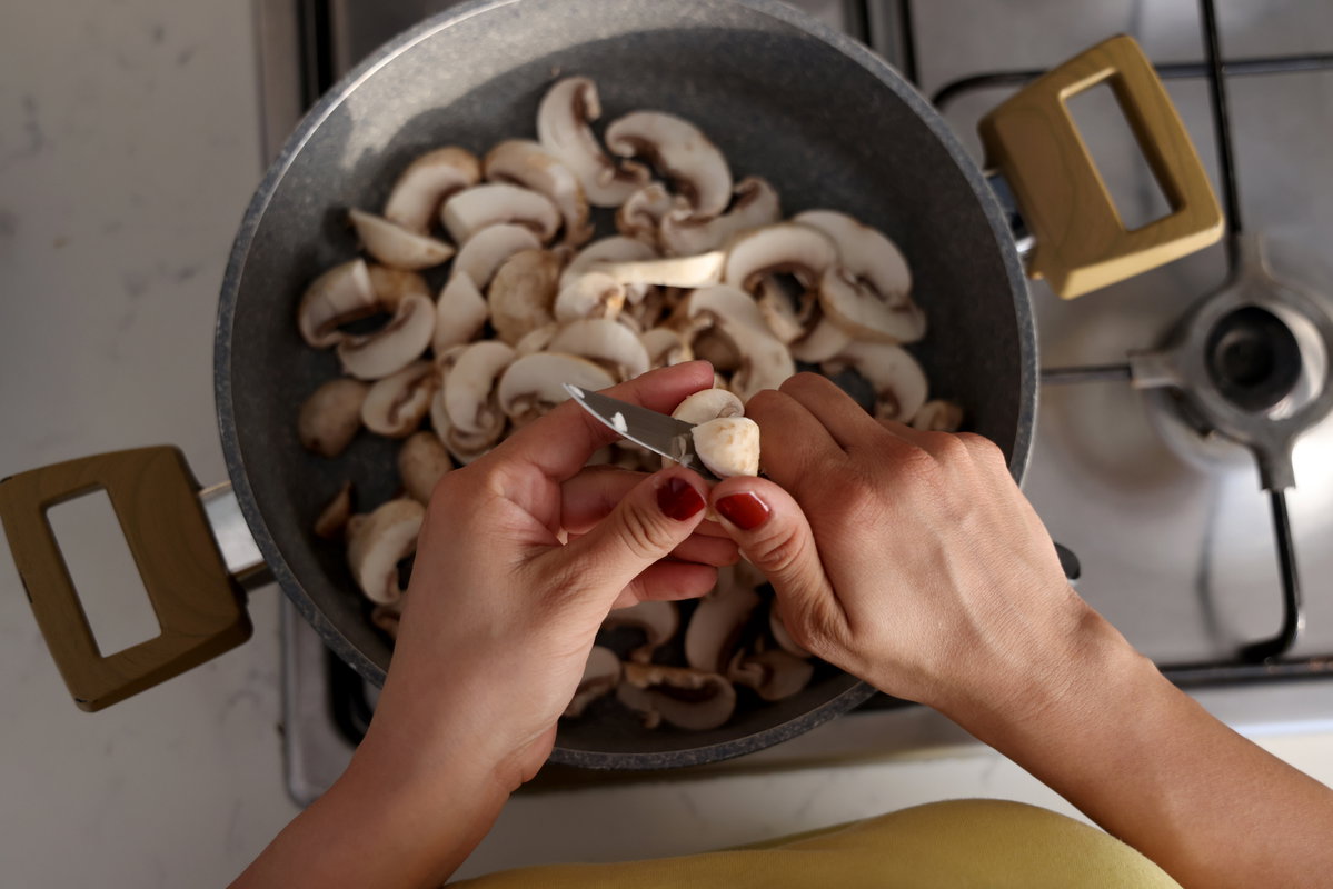 Frau schneidet Champignons in eine Pfanne.