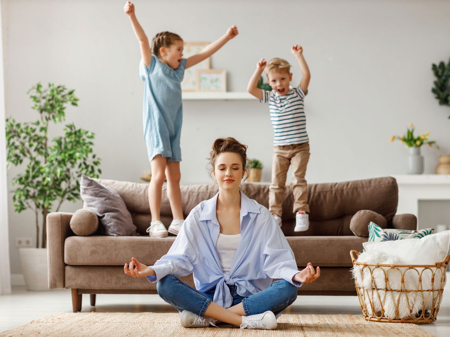 Kinder springen auf dem Sofa, Mutter meditiert.