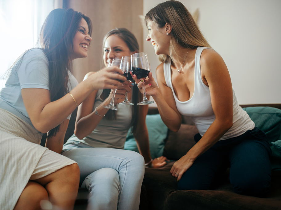 Ein par Freundinnen sitzen auf dem Sofa und stoßen mit einem Glas Rotwein an.