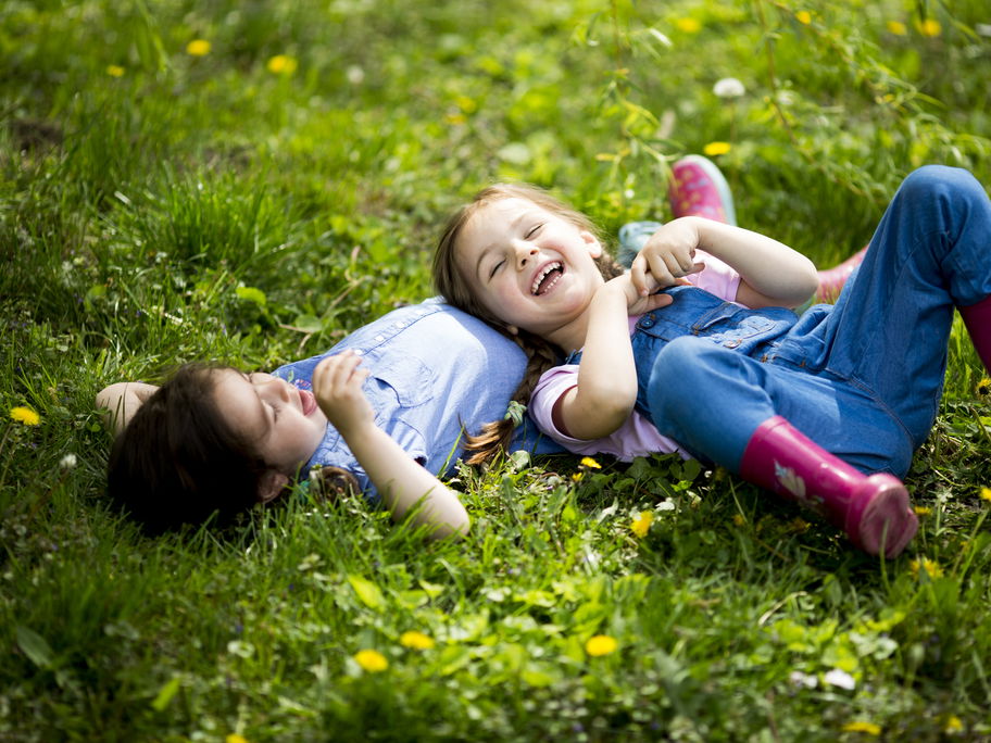 Zwei Kinder liegen auf einer grünen Wiese.