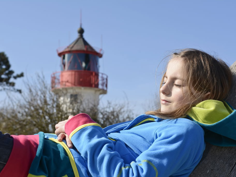 Mädchen chillt vor einem Leuchtturm.