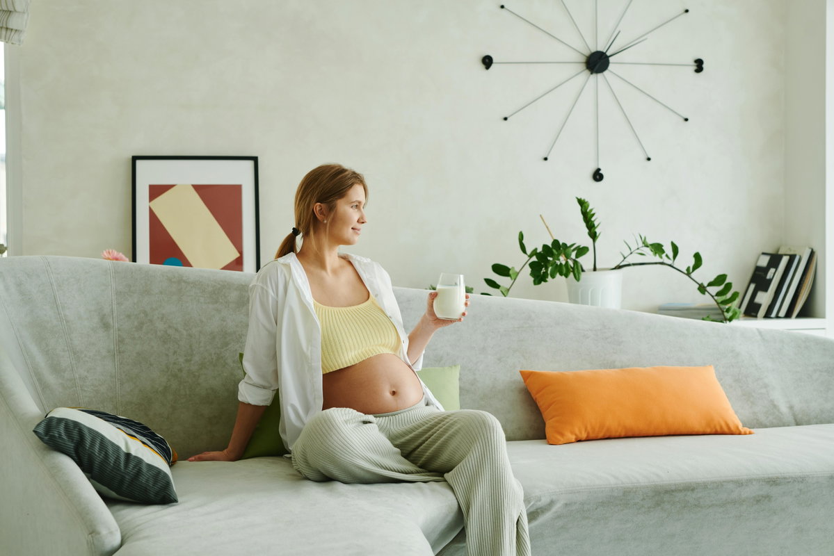 Schwangere Frau trinkt Buttermilch auf dem Sofa.