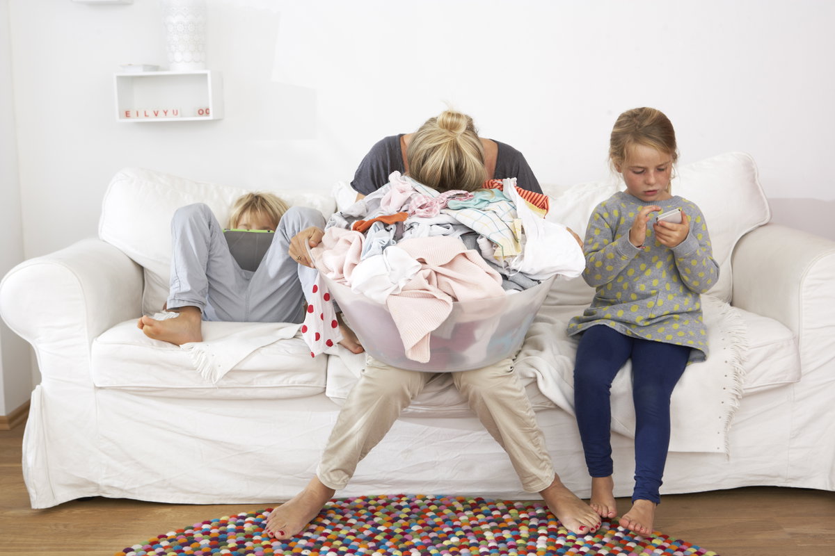 Erschöpfte Mutter Wäschekorb auf dem Schoß auf dem Sofa.