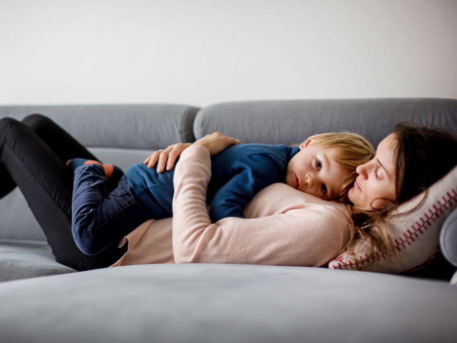 Mutter hält krankes Kind, liegen zusammen auf einer Couch.