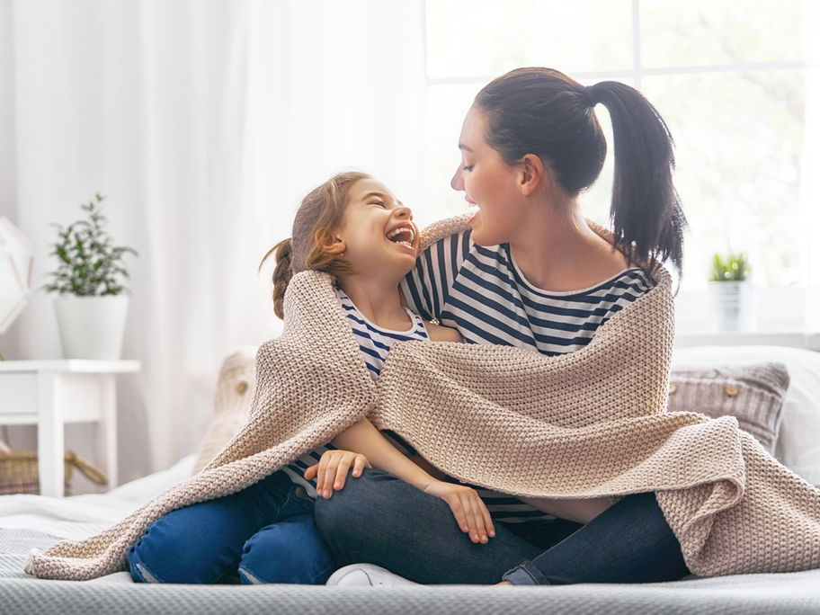 Mutter und Tochter sitzen lachend auf dem Sofa.