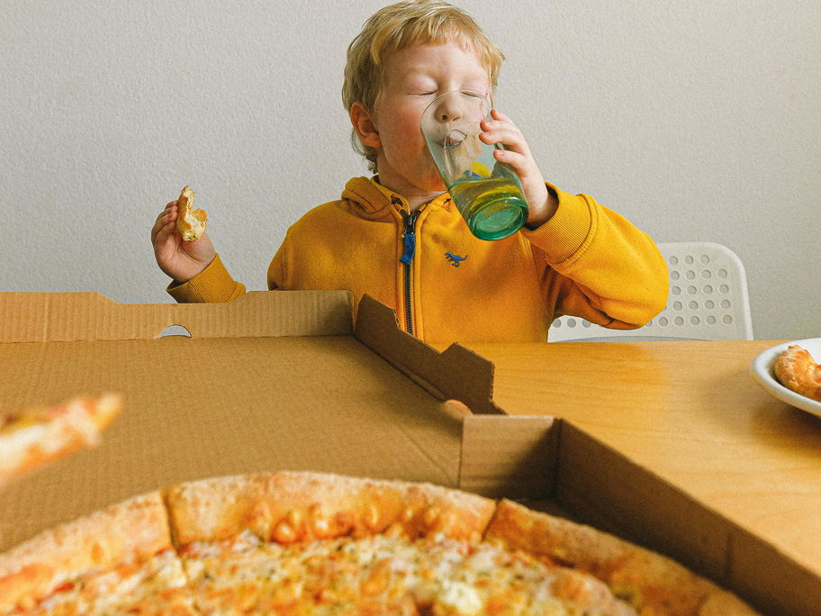 Kind isst Pizza aus Karton
