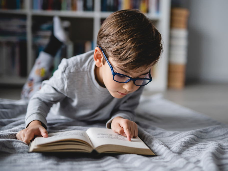 Junge, der auf dem Boden liegt und ein Buch liest.
