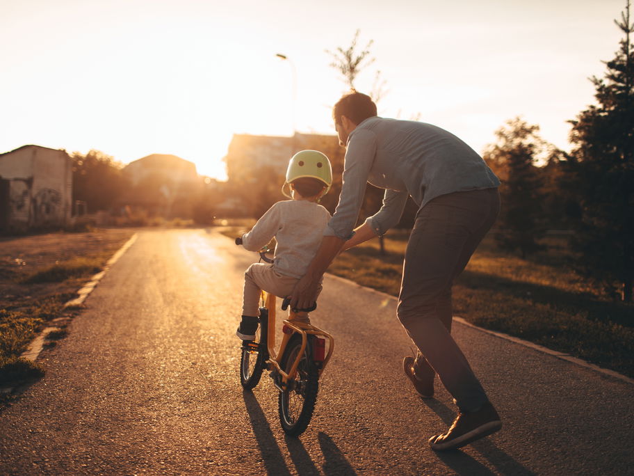 Vater hilft Kind beim Fahrradfahren lernen.