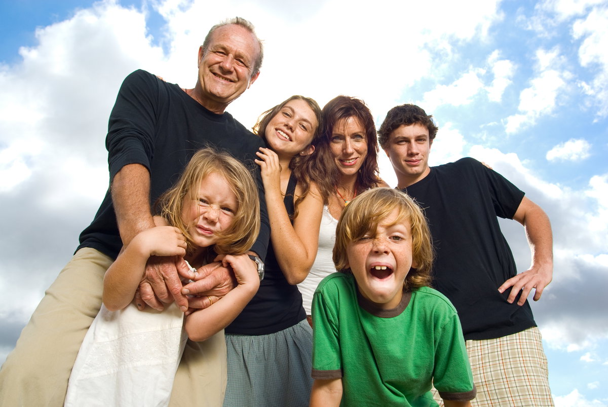Patchworkfamilie mit vier Kindern vor blau-wolkigem Himmel.